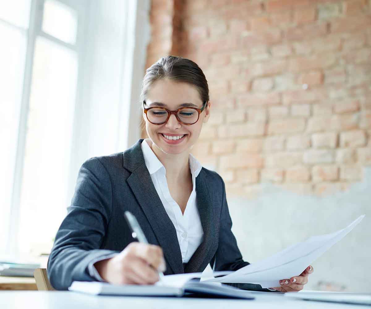 Caucasian woman in glasses smiles and writes in a notebook