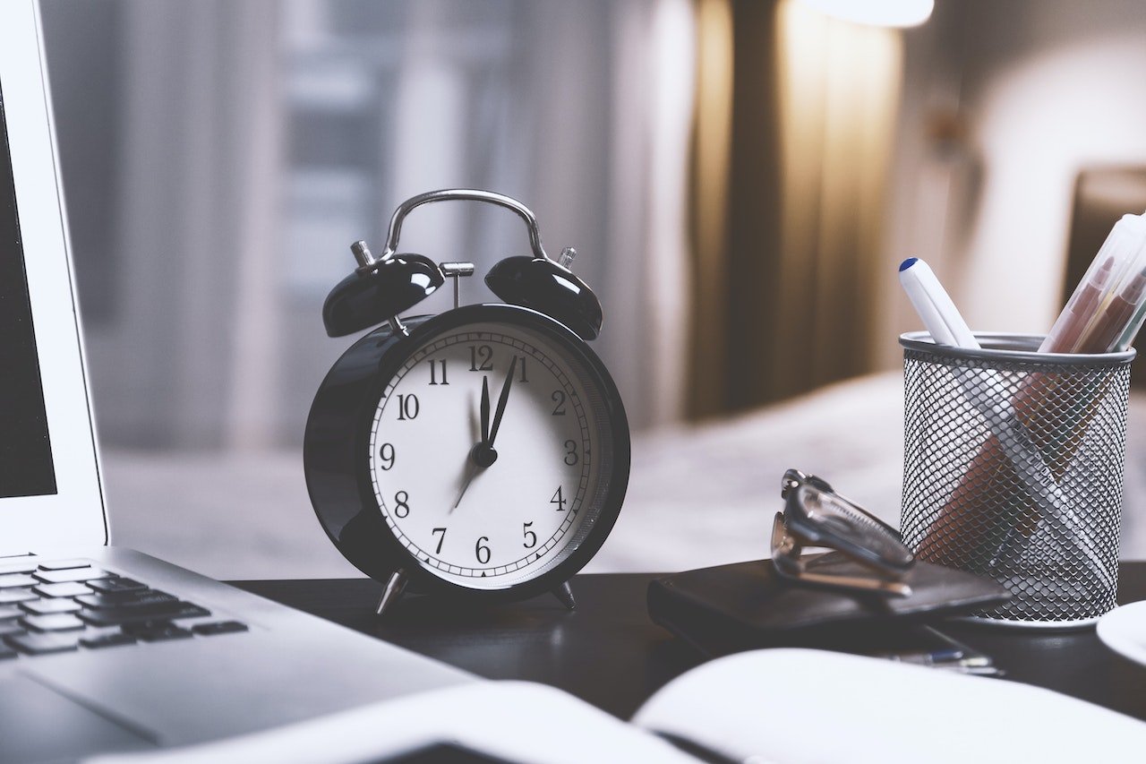 clock next to computer and pens on desk