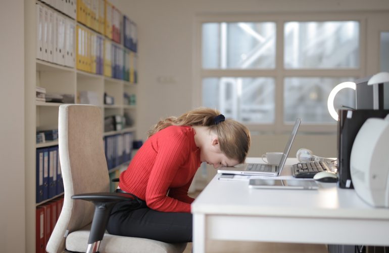 Woman sitting with head on her desk and laptop open.