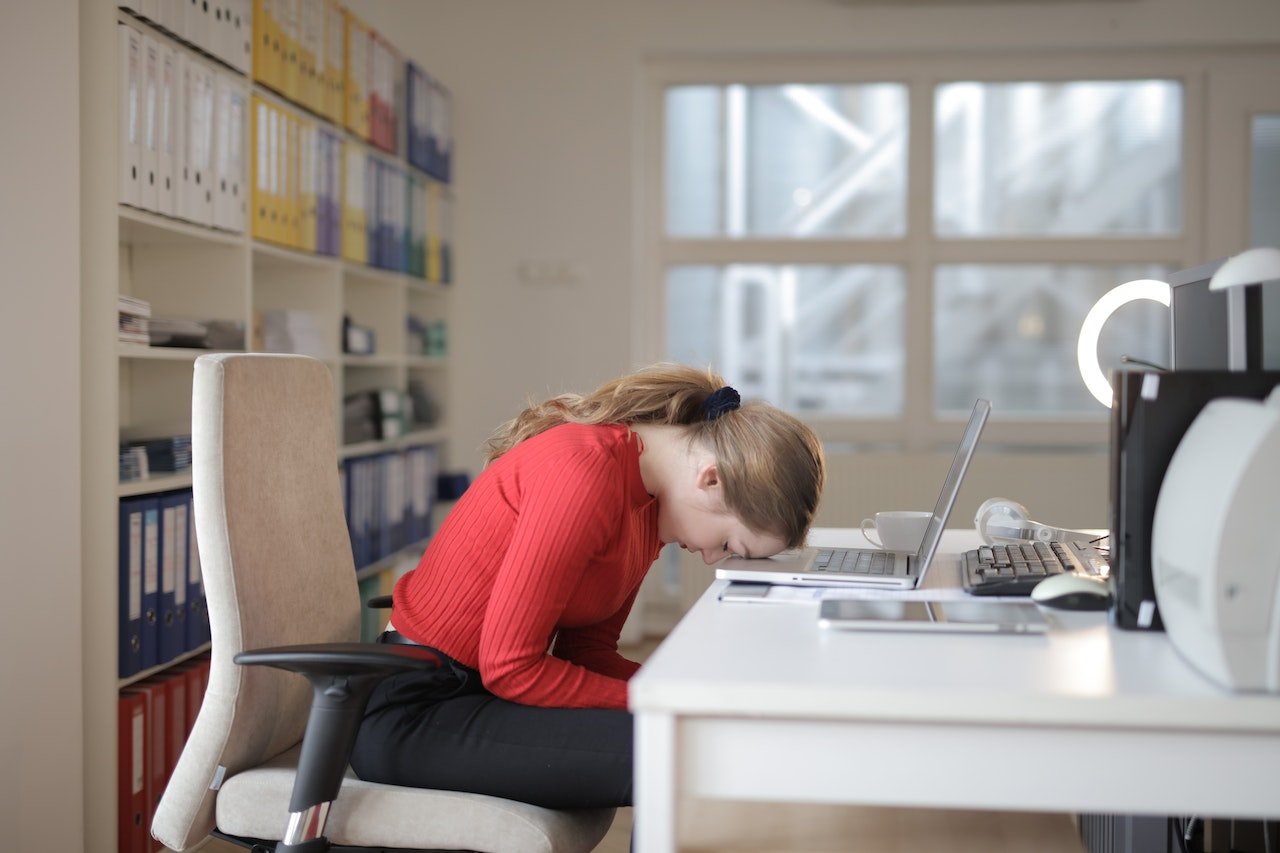 Woman sitting with head on her desk and laptop open.