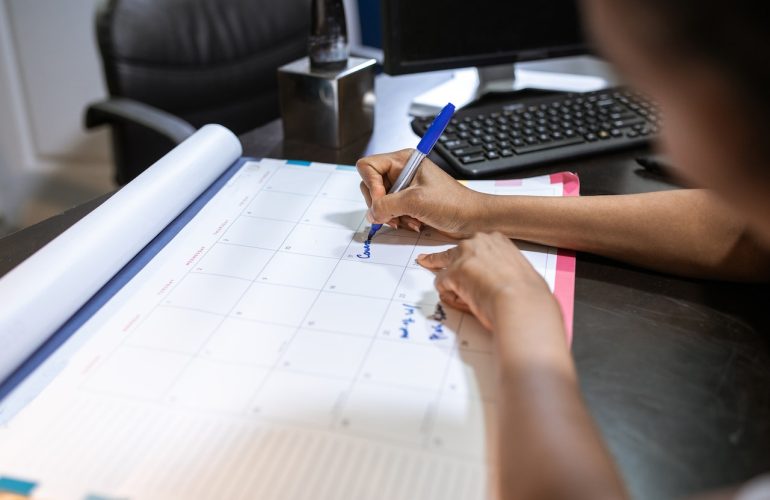 Person filling out desk calendar next to computer
