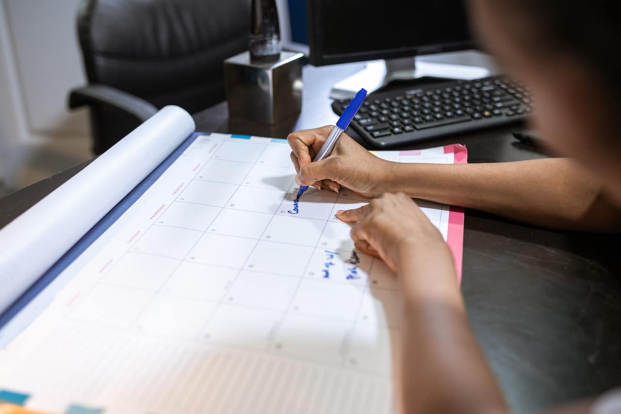 Person filling out desk calendar next to computer