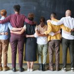 People standing in line with backs facing the camera and arms around each other.